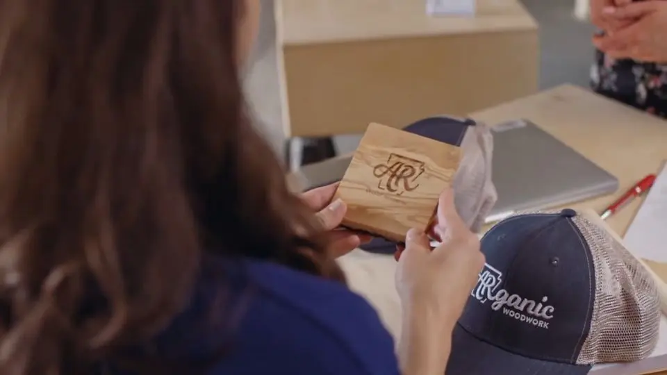Osoba drzi drveni promo proizvod sa logotipom dok su na stolu kacketi i kancelarijski materijal