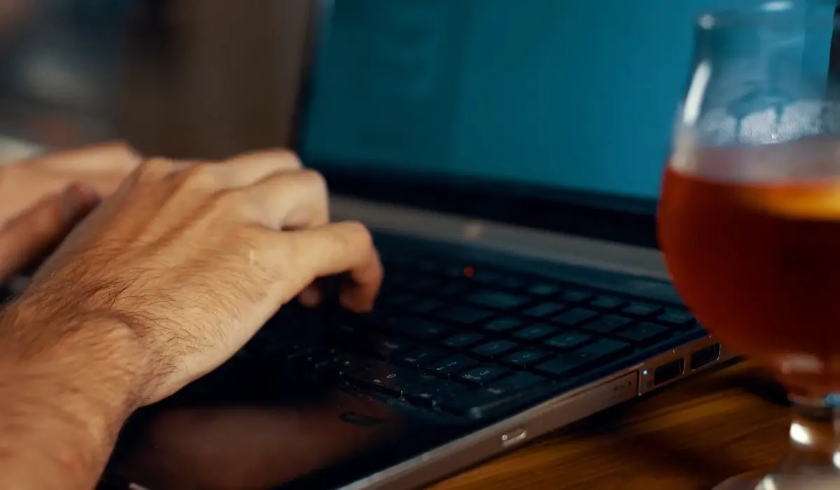 Reklamni materijal za hotele, restorane i kafiće - šta najviše ostavlja utisak 8 Osoba kuca na laptopu pored čaše pića u opuštenom radnom ambijentu.