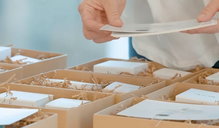 Ruke koje slažu luksuzne korporativne poklon pakete sa personalizovanim detaljima.