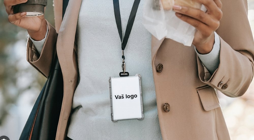 Osoba u poslovnoj odeći nosi ID držač sa natpisom „Vaš logo“ dok u rukama drži kafu i užinu.