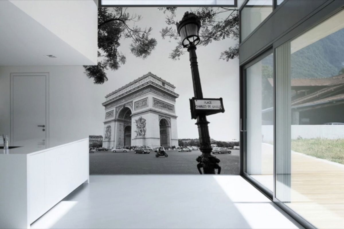 Crno-bela foto tapeta sa motivom Trijumfalne kapije u Parizu postavljena na zidu modernog, svetlog enterijera sa staklenim panelima.