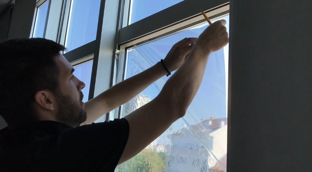 Osoba pažljivo nanosi samolepljivu foliju na prozor koristeći olovku za poravnavanje ivica.