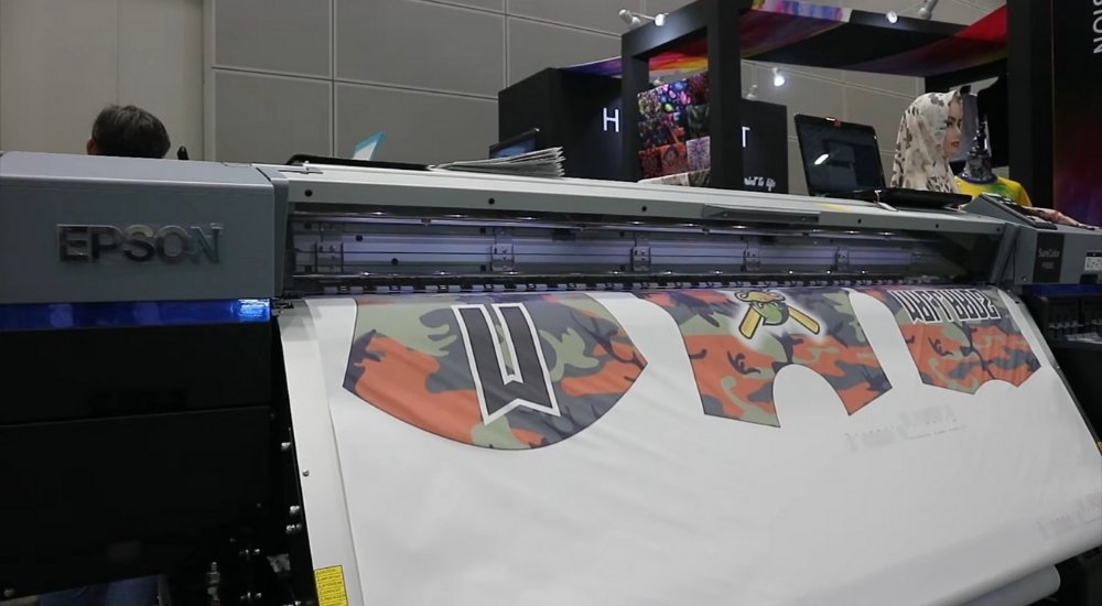 Digitalni Epson štampač u procesu štampe na tekstilu sa kamuflažnim uzorkom i slovima, na sajmu štamparske opreme.