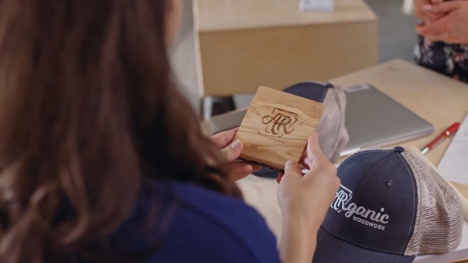 Osoba drzi drveni promo proizvod sa logotipom dok su na stolu kacketi i kancelarijski materijal