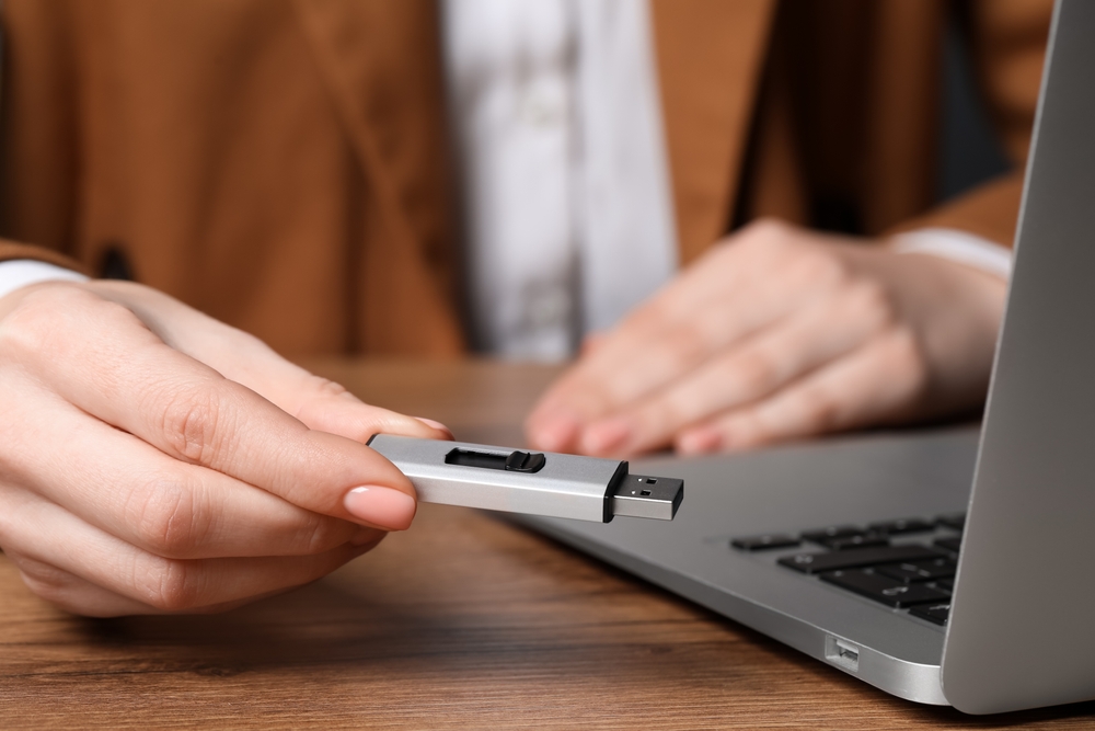 Osoba drži USB memoriju pored laptopa tokom prenosa fajlova i poslovnog rada